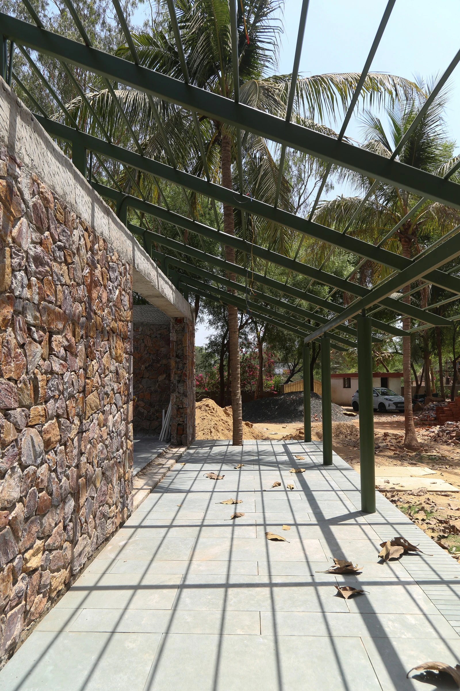 Random rubble stone masonry wall under sloping steel roof rafters during construction