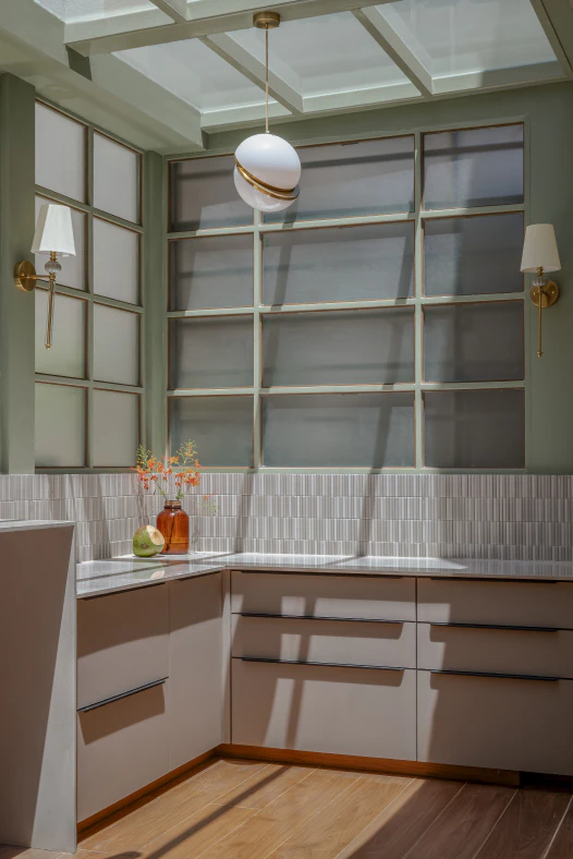 Sunlit kitchen nook beneath a skylight with frosted grid windows, brass wall sconces, and fluted tile splashback
