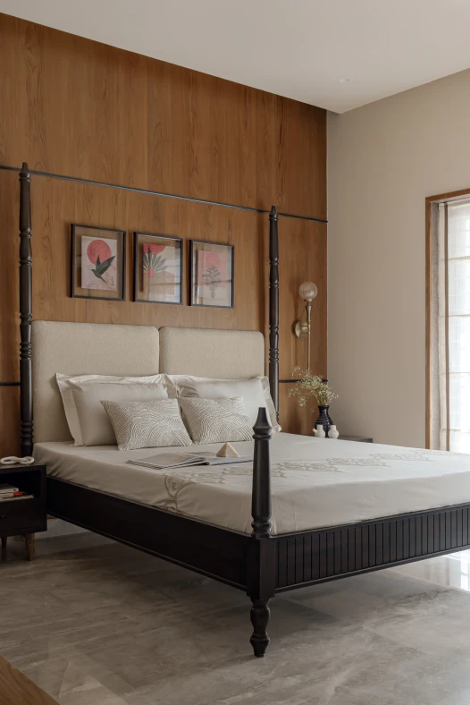 Four-poster dark timber bed with cream upholstered headboard, brass wall sconce, and framed art against wood paneling