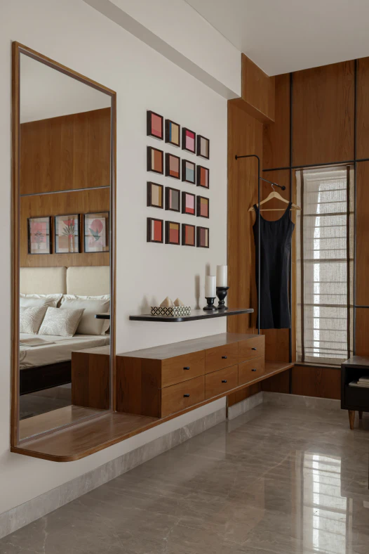 Bedroom dressing area with a full-length wall mirror, floating wooden drawer console, hanging rack, and framed artwork gallery