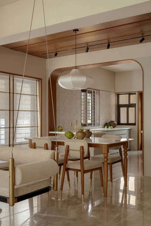 Dining area framed by an arched timber opening with a marble dining table, fabric pendant lamp, and brass-accented chairs